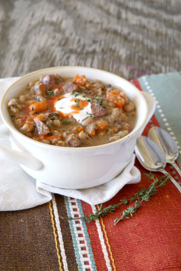 white soup crock filled with black eyed pea soup made in a slow cooker, sitting on top of a brown and red cloth place mat