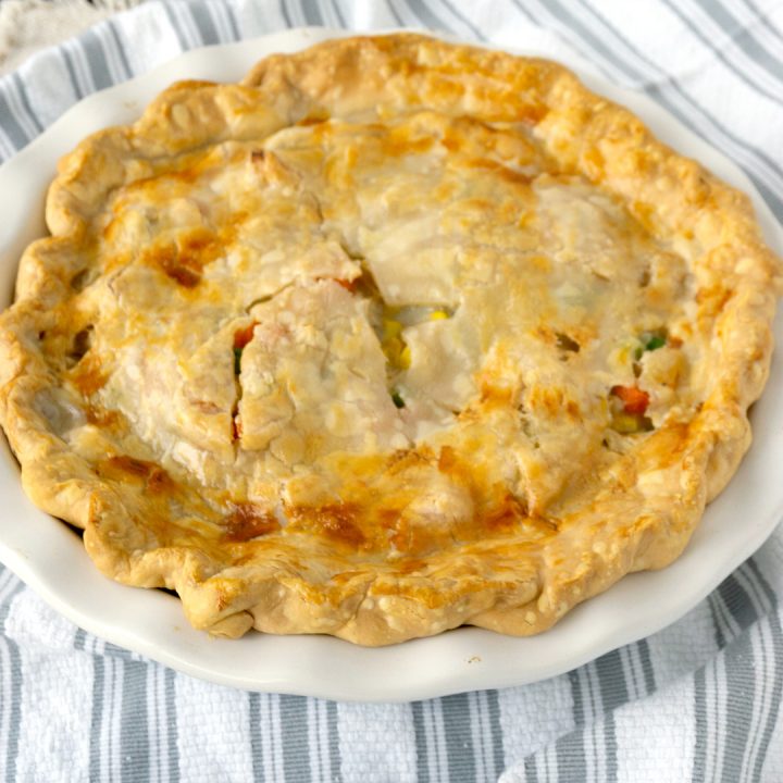 turkey pot pie with pie crust in a white baking dish on a striped towel