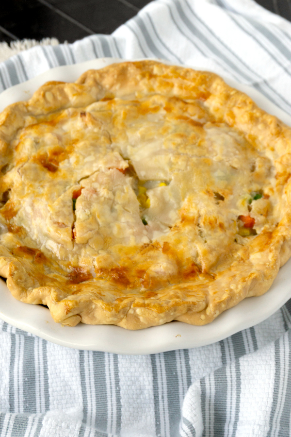 turkey pot pie with pie crust in a white baking dish on a striped towel