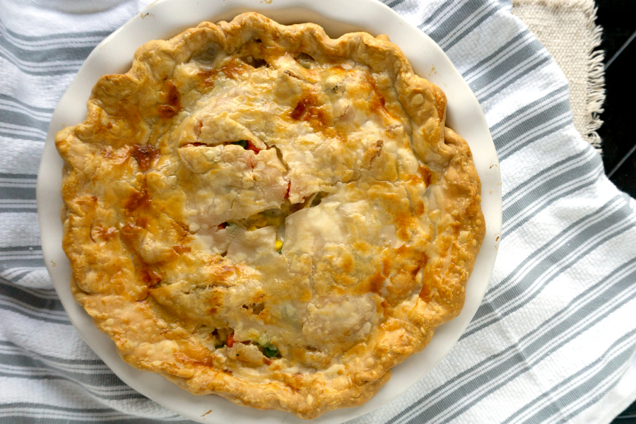 turkey pot pie with pie crust in a white baking dish on a striped towel