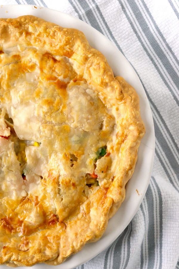 turkey pot pie with pie crust in a white baking dish on a striped towel