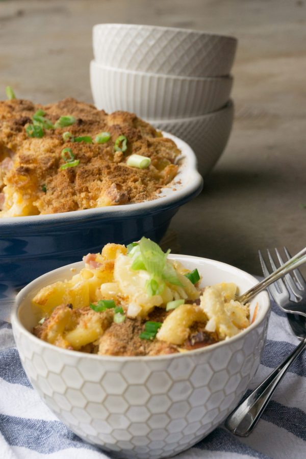 ham and macaroni casserole in a white serving bowl with a pan of the casserole behind it.