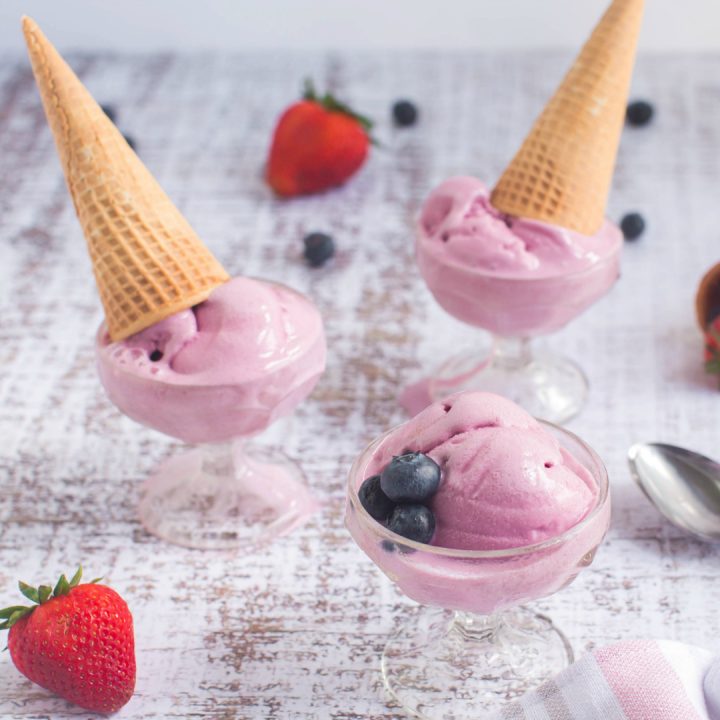scoops of pink frozen dessert in glass cups with sugar cones on top