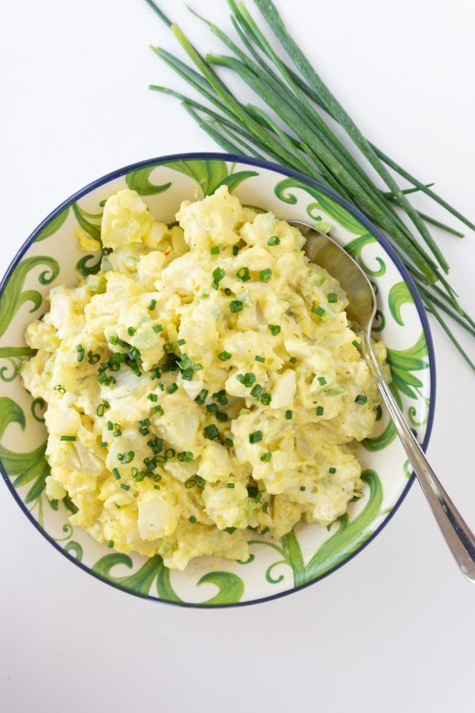 overhead photo of mustard potato salad in floral serving bowl garnished with snipped chives