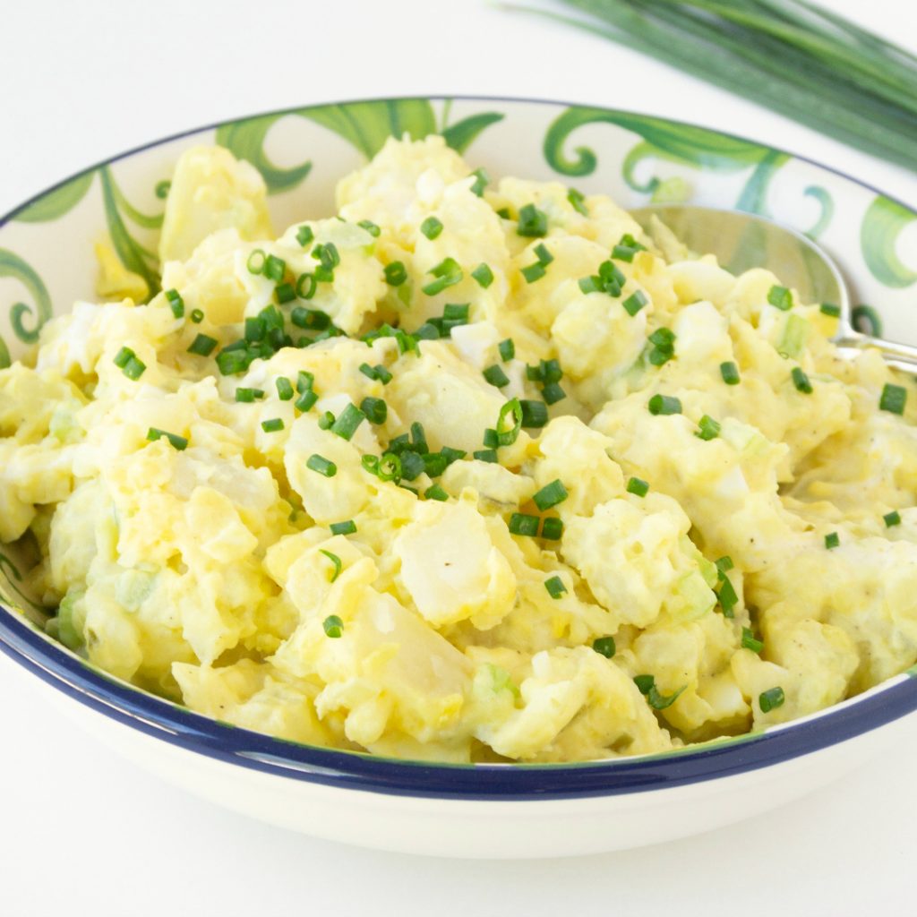 close up photo - bowl of simple potato salad topped with fresh chives