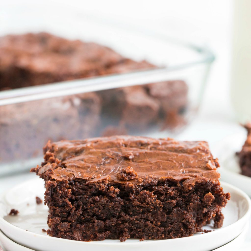 fudgy coconut oil brownie on white plate with pan of brownies in background