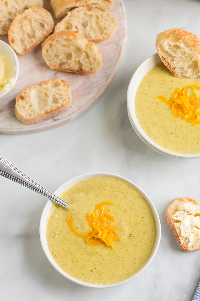 overhead photo: 2 bowls of cheddar broccoli soup next to slices of French bread