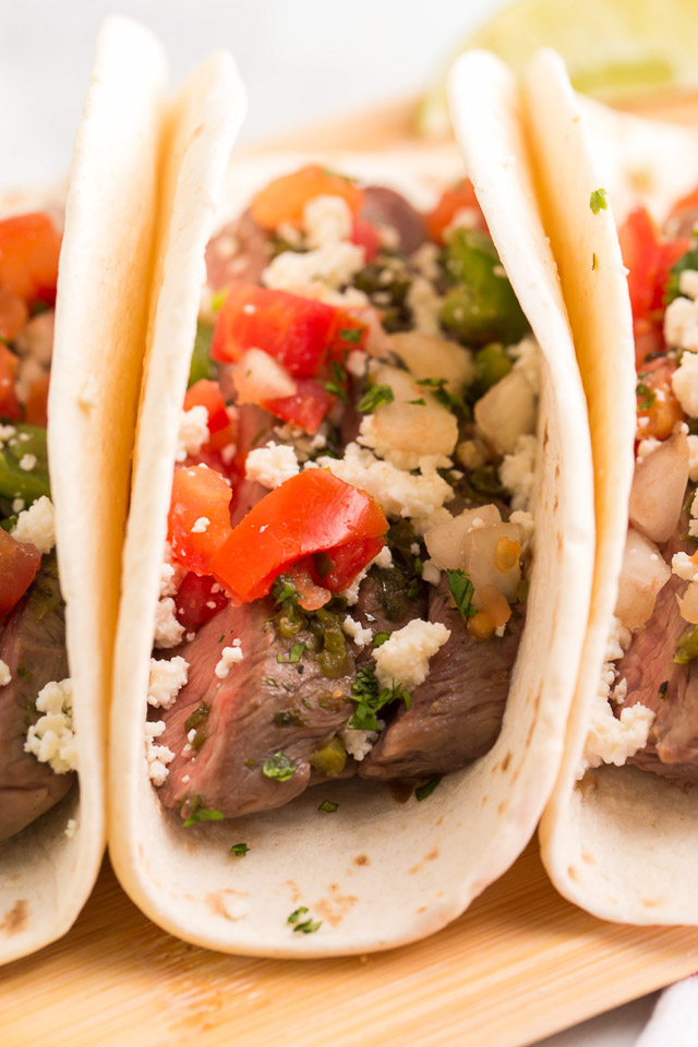 close up image of steak taco with diced tomatoes, crumbly Mexican cheese and seasonings