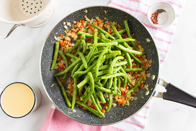 overhead photo: fresh green beans cooking in in a skillet with diced onions and bell peppers