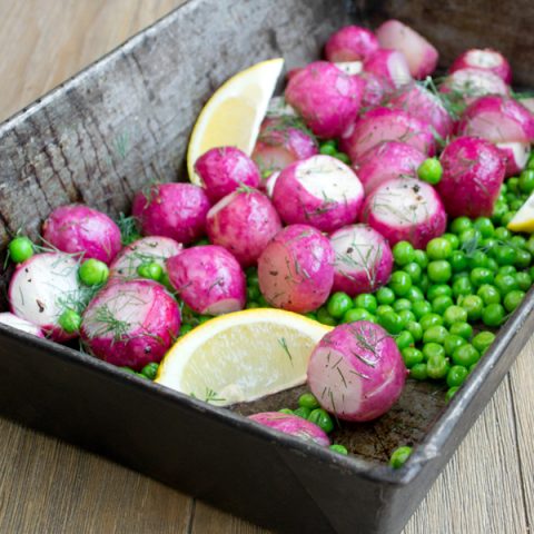 pan of oven-roasted radishes with peas, lemon wedges, and fresh dill