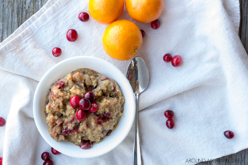 white bowl with orange cranberry oatmeal surrounded by fresh oranges and cranberries