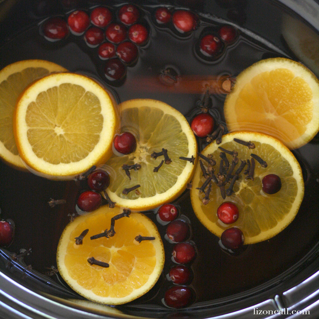 a slow cooker full of warm party punch with orange slices, fresh cranberries, and cloves