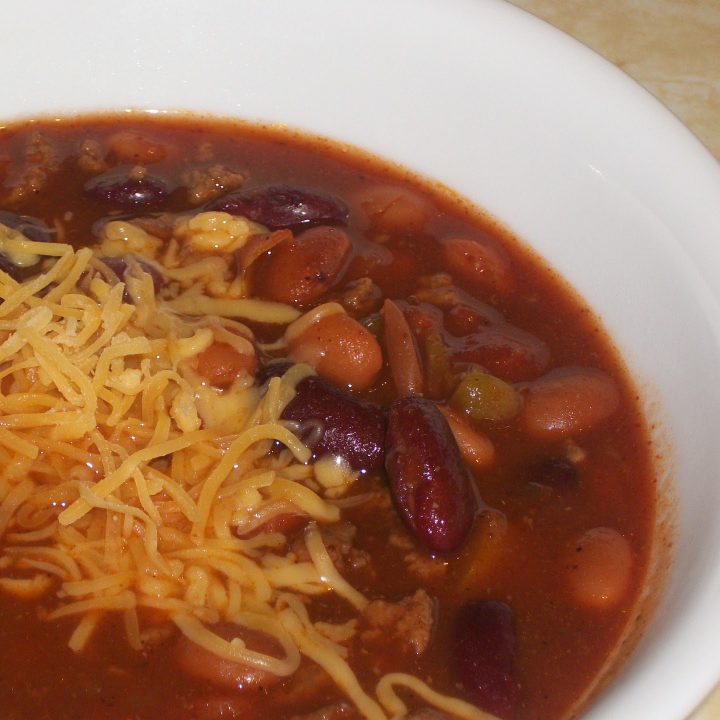 bowl of slow cooker 10 can chili topped with shredded cheddar cheese