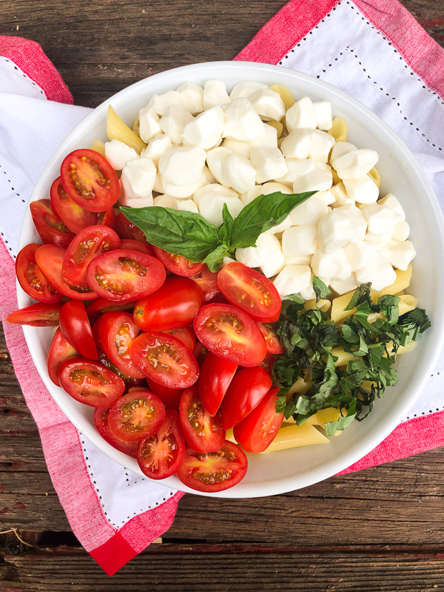 pasta in a white bowl with tomatoes, basil and cheese