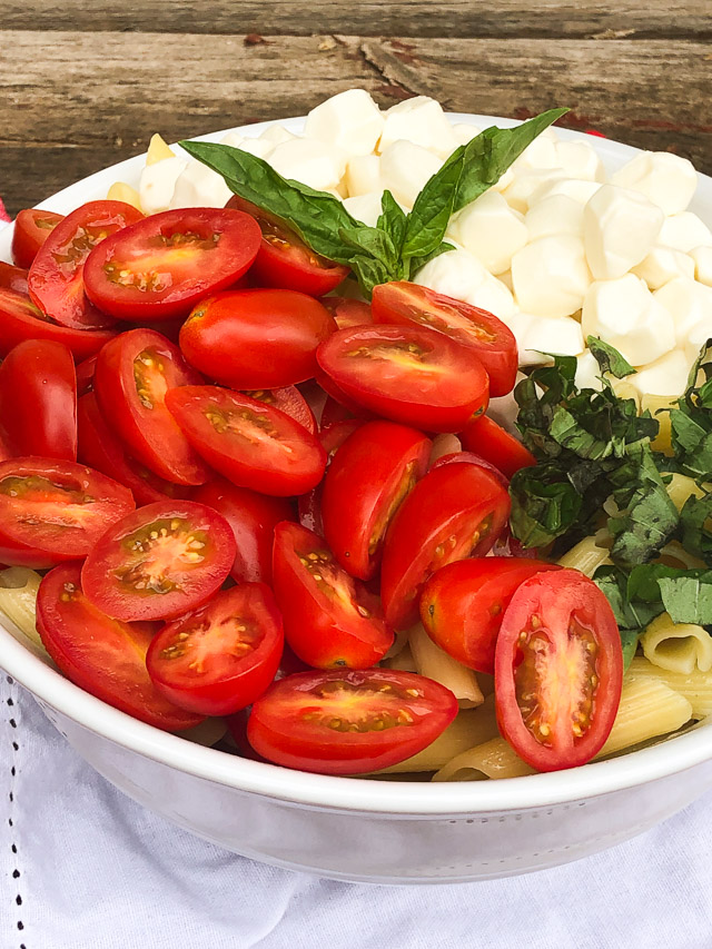 pasta in a white bowl with tomatoes, basil and cheese