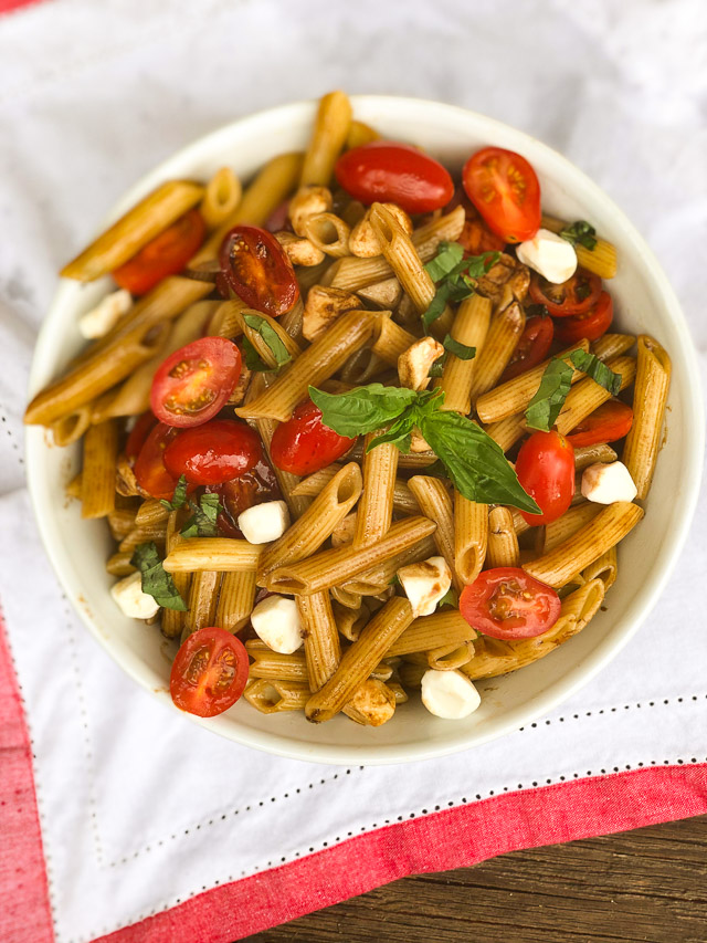 pasta in a white bowl with tomatoes, basil and cheese