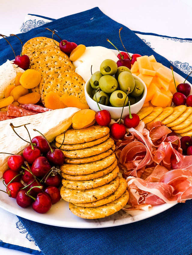 charcuterie board on a white platter with summer cherries, cantaloupe, meats & cheeses