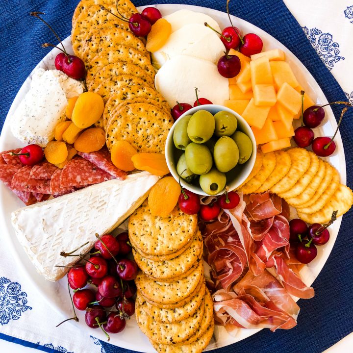 charcuterie board on a white platter with summer cherries, cantaloupe, meats & cheeses