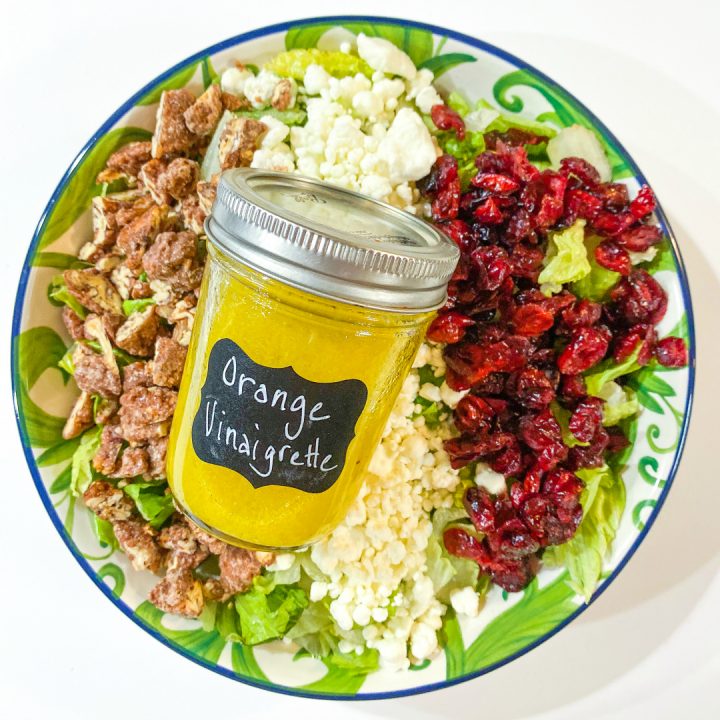 Cranberry, Goat Cheese, & Pecan Salad with Orange Vinaigrette in a bowl with a jar of dressing