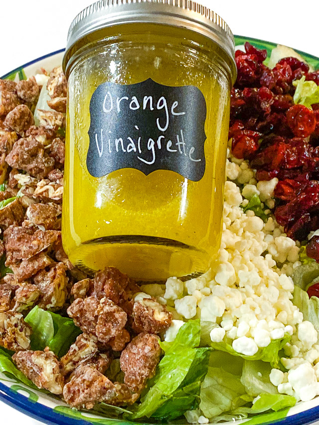 Cranberry, Goat Cheese, & Pecan Salad with Orange Vinaigrette in a bowl with a jar of dressing
