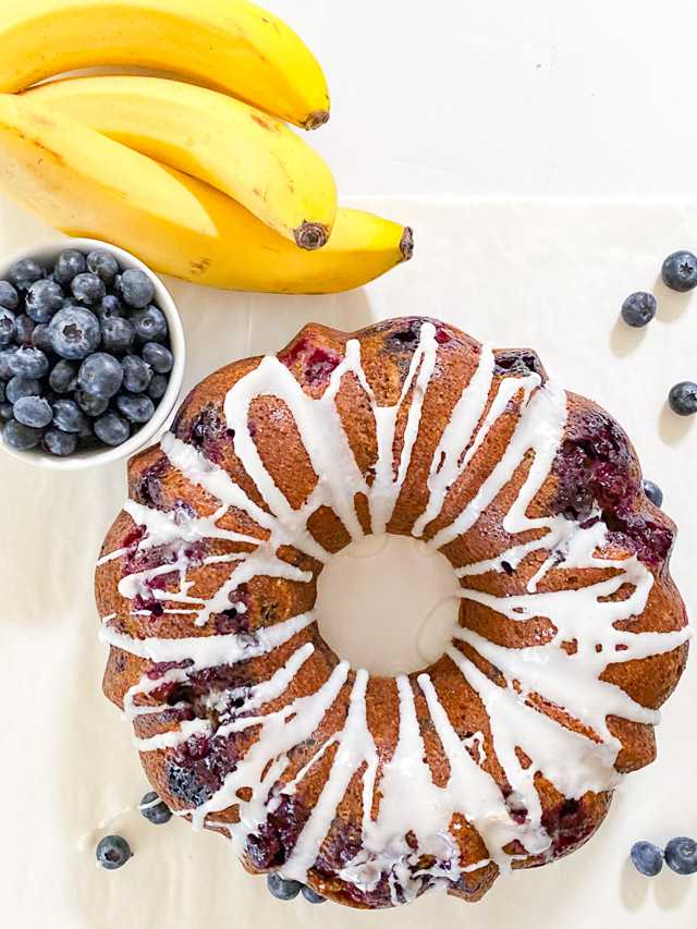 blueberry banana bread on white table with bananas and blueberries