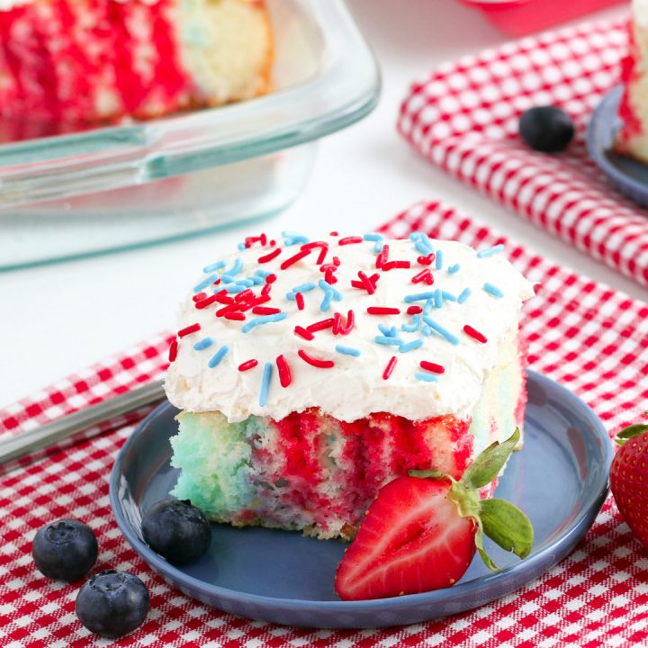 4th of July Poke Cake with berries on a white table with red checkered napkins