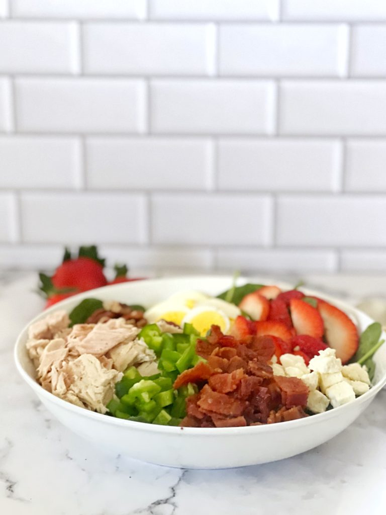 Keto Chicken, Bacon, & Spinach Salad in a white bowl with strawberries, egg, and feta