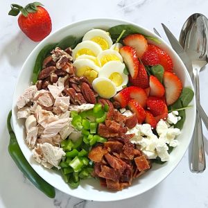 Keto Chicken, Bacon, & Spinach Salad in a white bowl with strawberries, egg, and feta