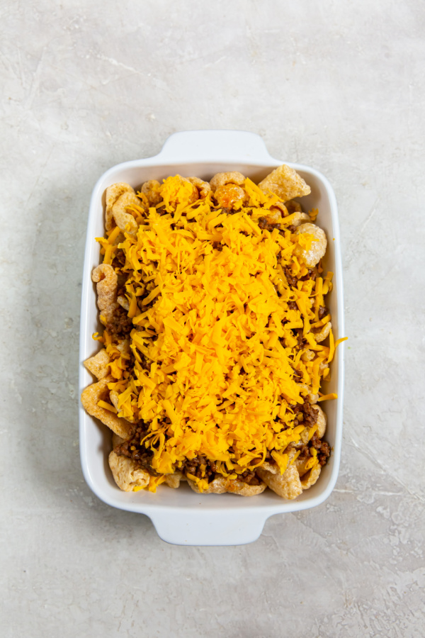 layering keto walking taco casserole ingredients in a white dish